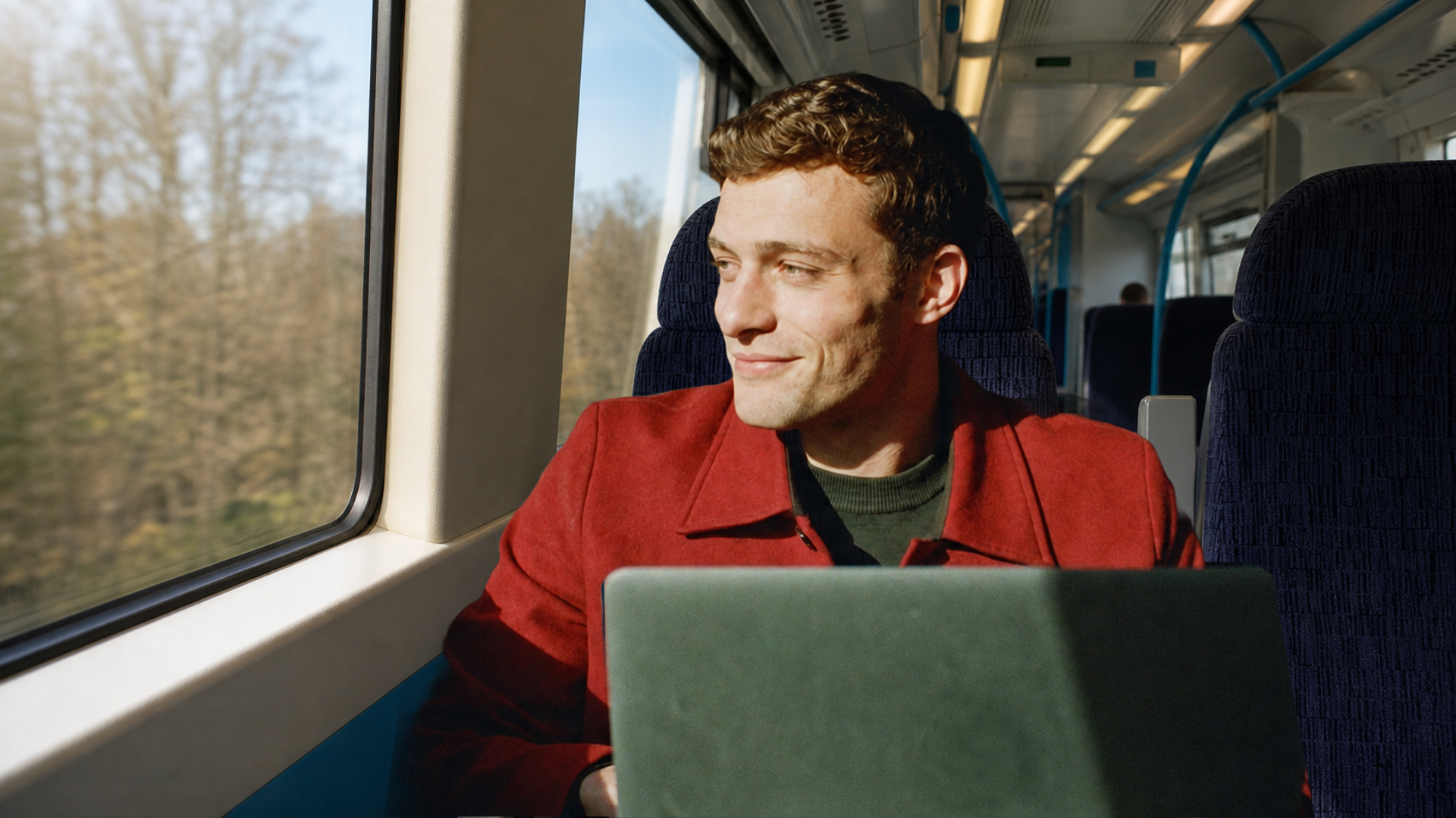 A writer in a red coat on a Southeastern train with his laptop open